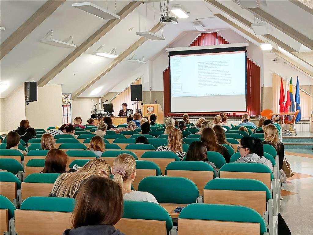 Uczestnicy zajęć siedzą w fotelach kinowych w auli CKZiU w Ostrołęce w tle prowadząca zajęcia i materiał wyświetlany na ekranie projekcyjnym